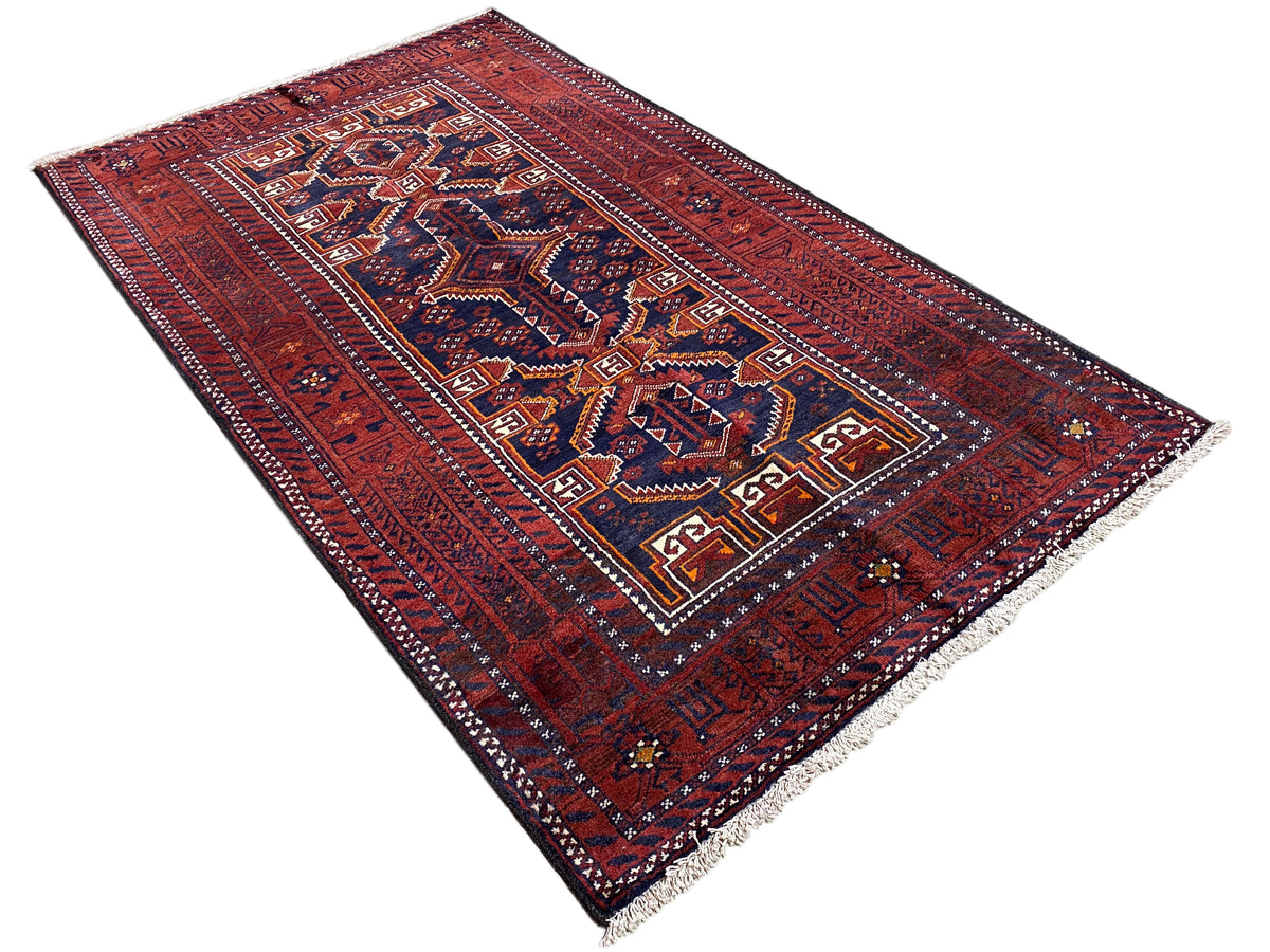 Rectangular Baluchi rug, red with a dense ornamental field in blue/white and a surrounding border.