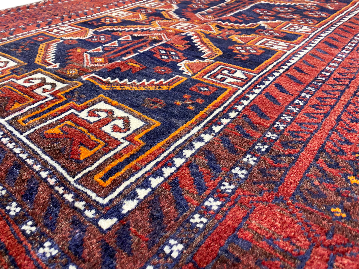 Baluch rug close-up: red-and-blue pattern with white and yellow decorative lines.