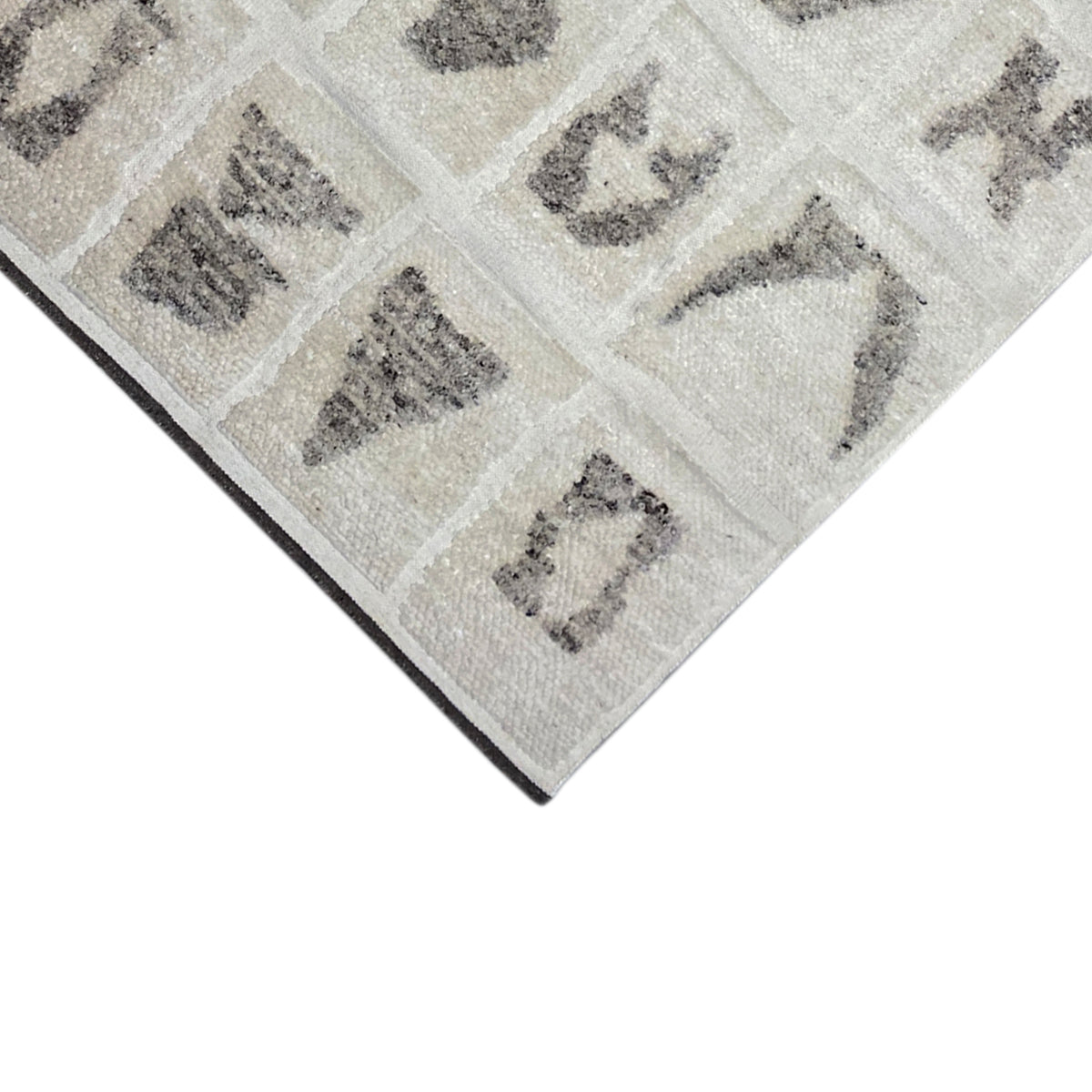 Corner of the Berber rug with a beige background, gray symbols, and a clean edge