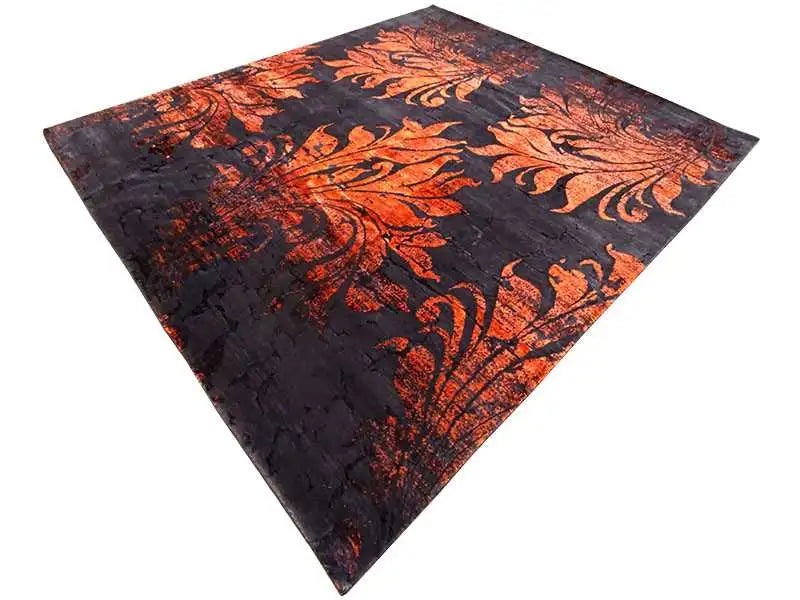 Designer rug with a dark surface and a large orange ornamental motif, positioned at an angle.