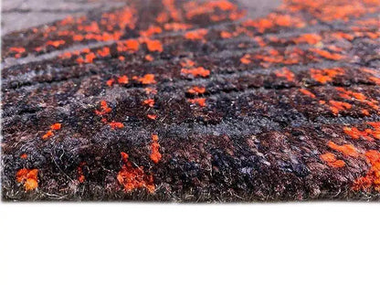 Close-up of a carpet surface: dark pile with orange paint splatters and texture.