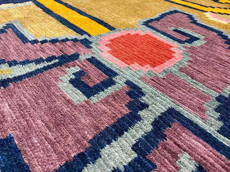 Designer rug with purple pile, red accents, and blue geometric border patterns