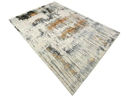 Designer rug from an angled close-up: light gray with faded stripes and ochre sections