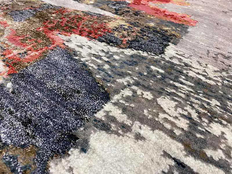 Carpet surface with a coarse, fluffy pile and contrasting brushstrokes in blue, red, and gray