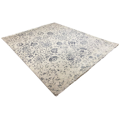 Corner view: Designer rug with a blue decorative pattern on a light background, appearing square-shaped