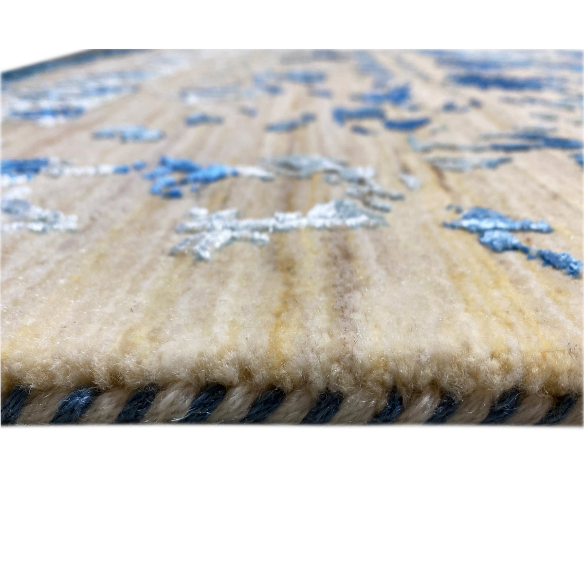 Close-up of carpet pile: beige pile with blue embellishments and dense fringe trim