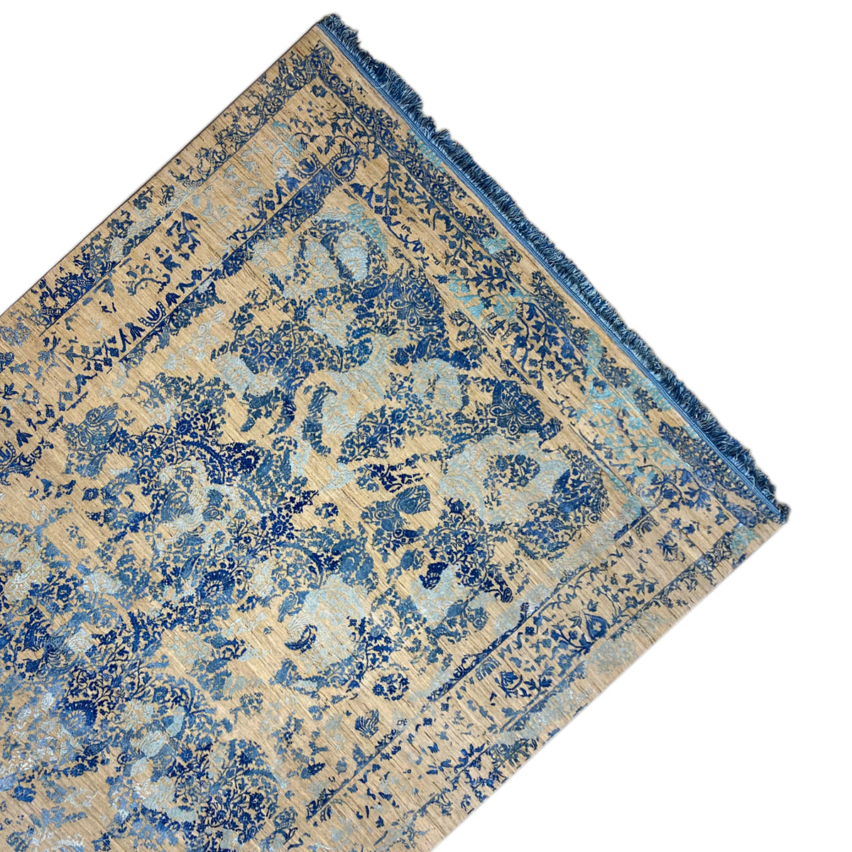 Corner of the rug with a blue ornament, beige background, and hemmed edge