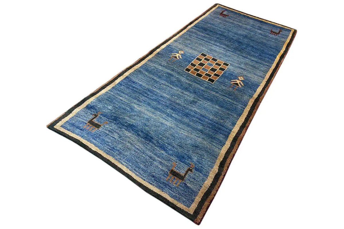 Blue Gabbeh rug with a beige border and central square pattern, lying diagonally