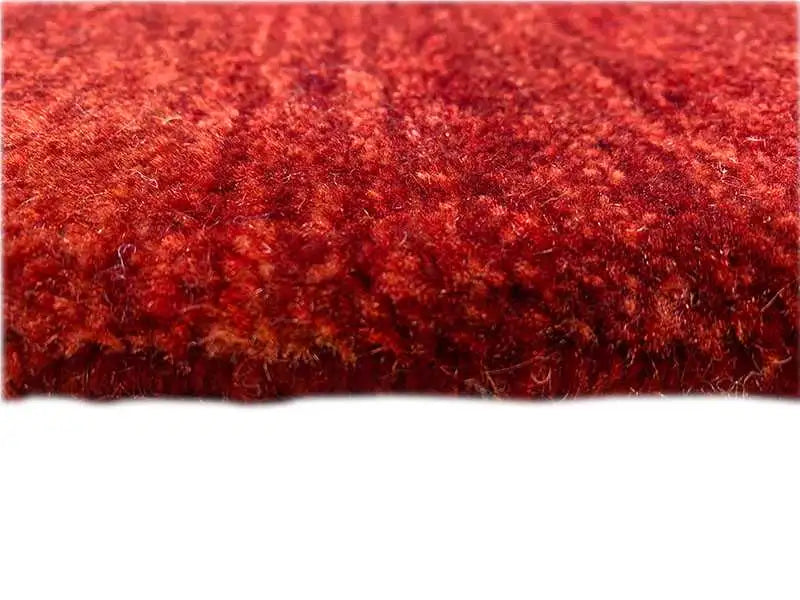 Close-up of a Gabbeh runner rug: dark red, densely sheared pile surface
