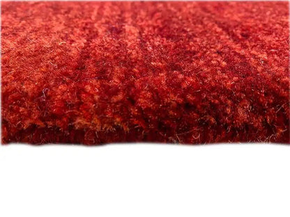 Close-up of a Gabbeh runner rug: dark red, densely sheared pile surface