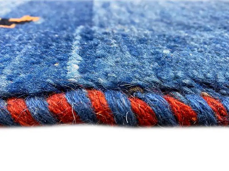 Detailed view of the carpet edge: blue pile bundle with red pattern elements, fringe
