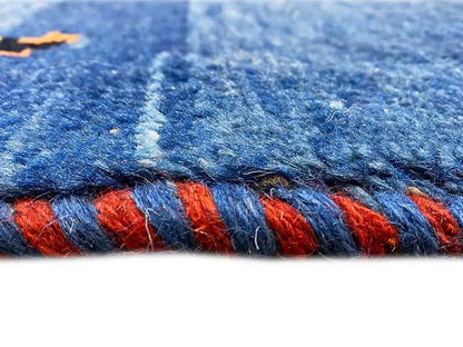 Detailed view of the carpet edge: blue pile bundle with red pattern elements, fringe
