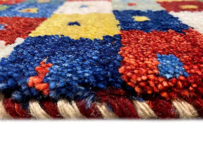 Gabbeh rug detail: colorful pile texture and fringes along the edge, with blue and red in the pattern.
