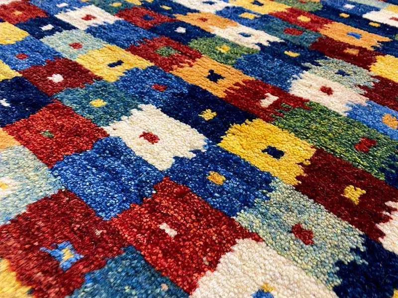 Gabbeh rug surface with a dense pile and colorful squares in blue, red, yellow, and cream.