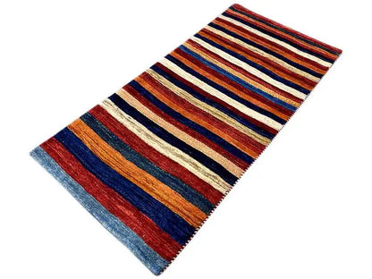 Gabbeh rug shown at an angle with orange-red and blue stripes on cream