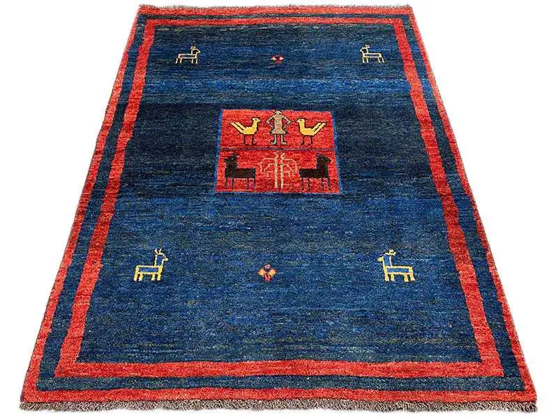 Gabbeh rug with a dark blue background, red border, and geometric central medallion