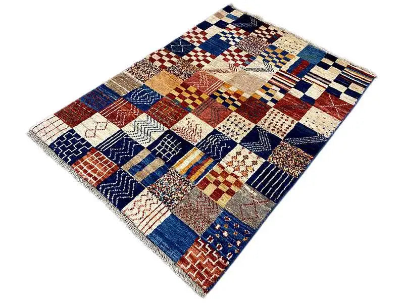 Rectangular Gabbeh rug with blue, red, and cream patchwork, with fringes along the edges