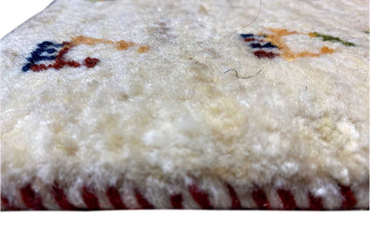 Close-up of a Gabbeh rug, cream-colored pile with a reddish-brown border and colorful motifs