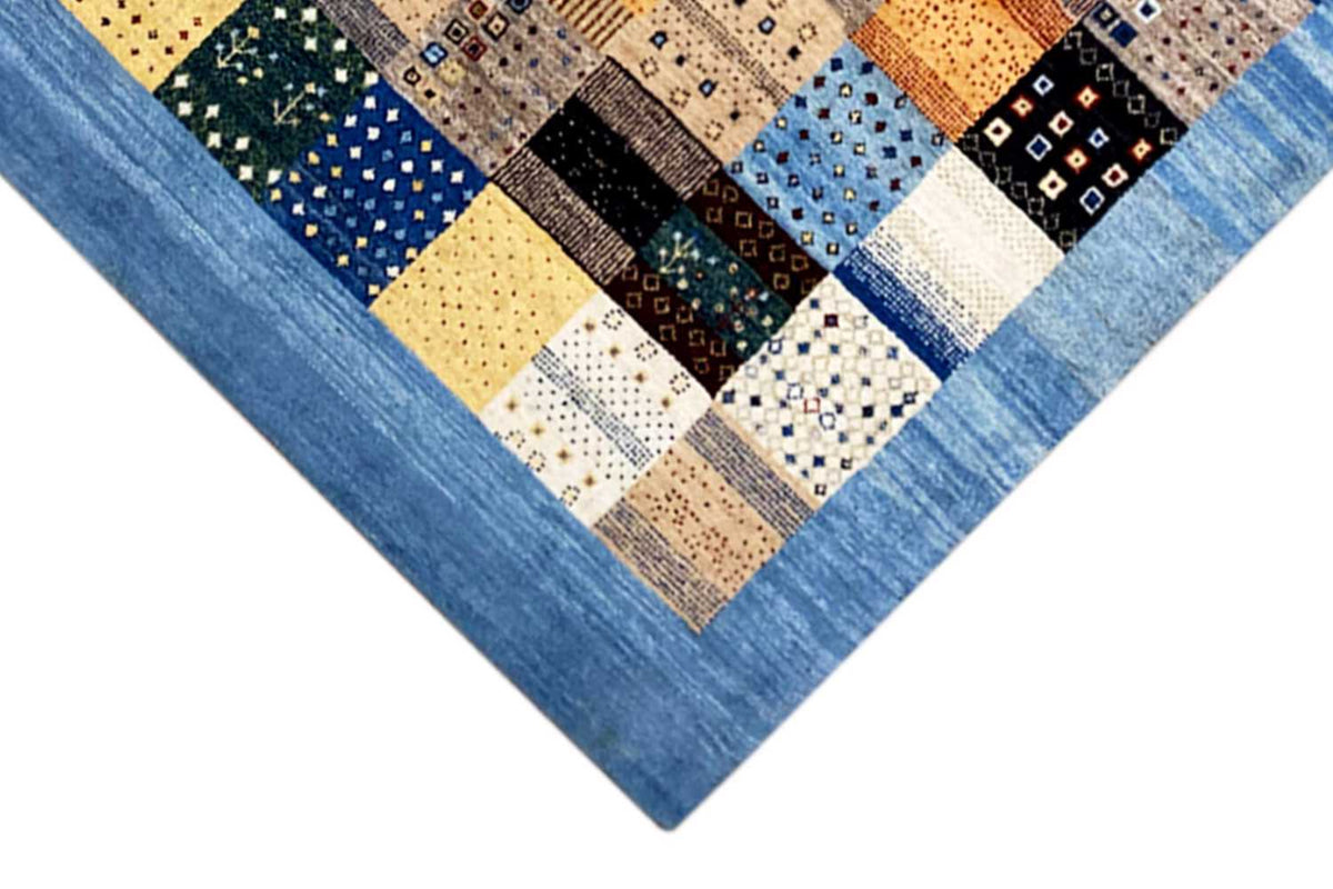Close-up detail of the rug: blue edging, patchwork of squares in yellow, blue, black, and beige