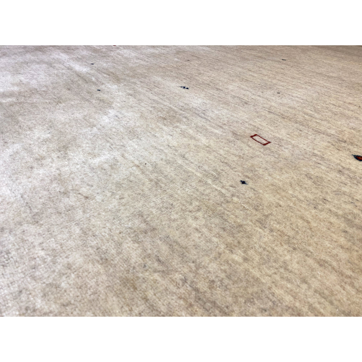 Close-up: beige carpet surface with a fine woven texture and colorful dots.