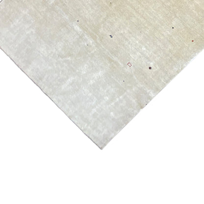 Corner of a beige Gabbeh rug with colorful dots and a short pile edge.