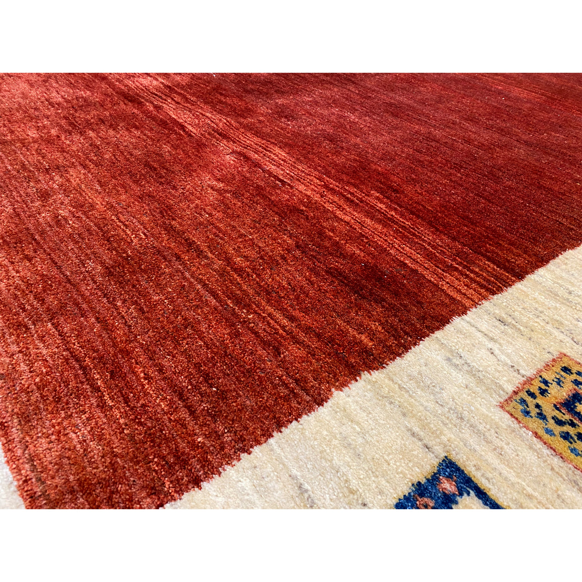 Gabbeh rug close-up: reddish-brown pile surface with a beige border area