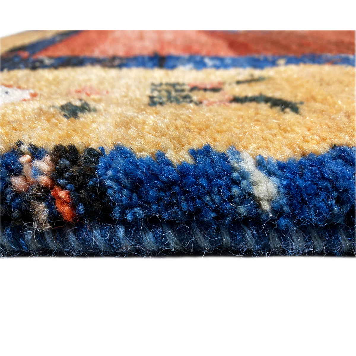 Close-up of the edge of a Gabbeh rug: dense blue pile and braided tassel