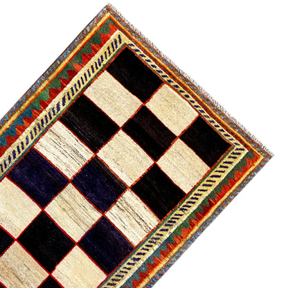 Gabbeh rug corner with a diamond pattern in cream, black and dark blue, colored border