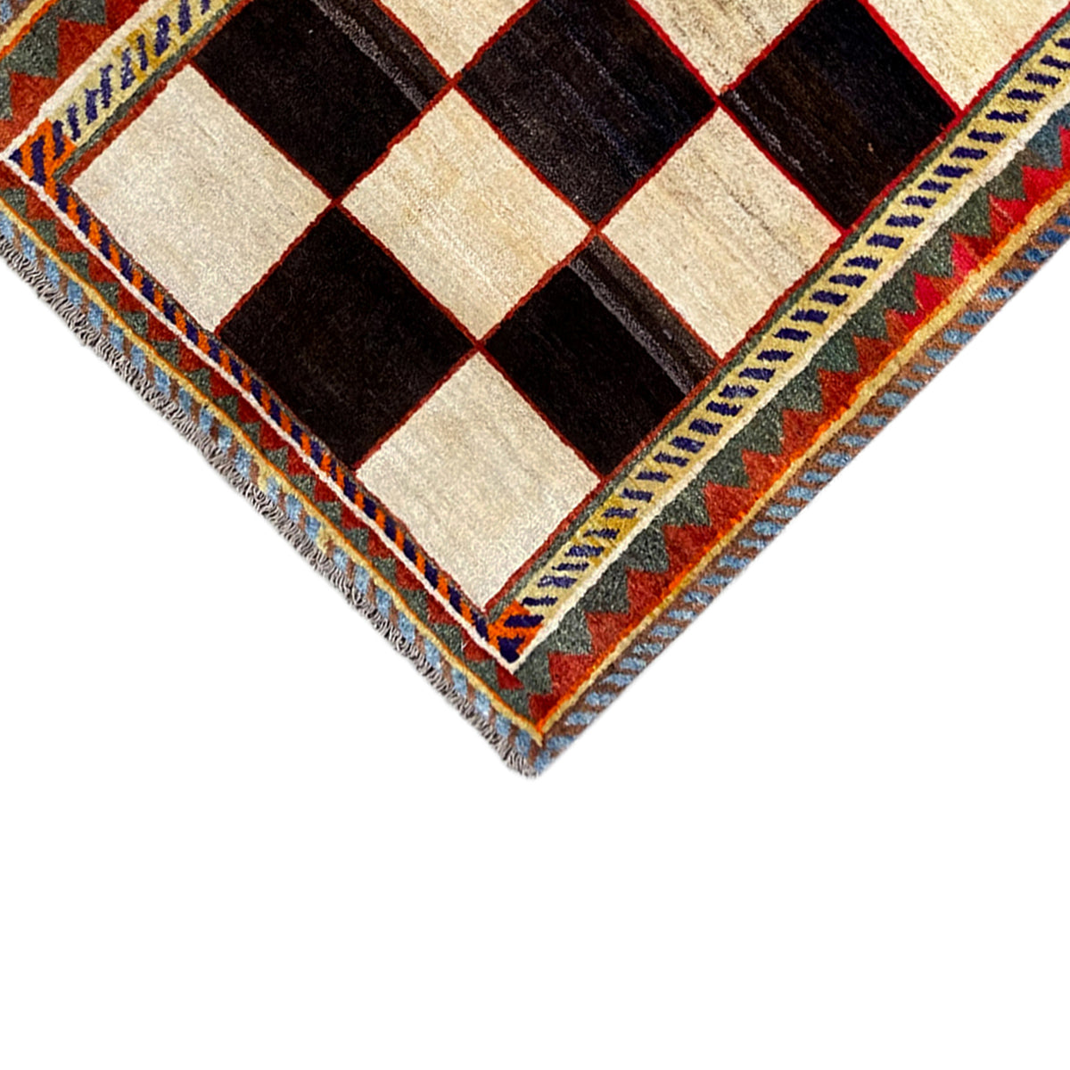 Gabbeh rug corner in close-up: cream and black diamond pattern, colorful border with fringes