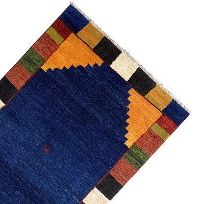 Rug corner with a border of colorful squares, a blue center, and short fringes.