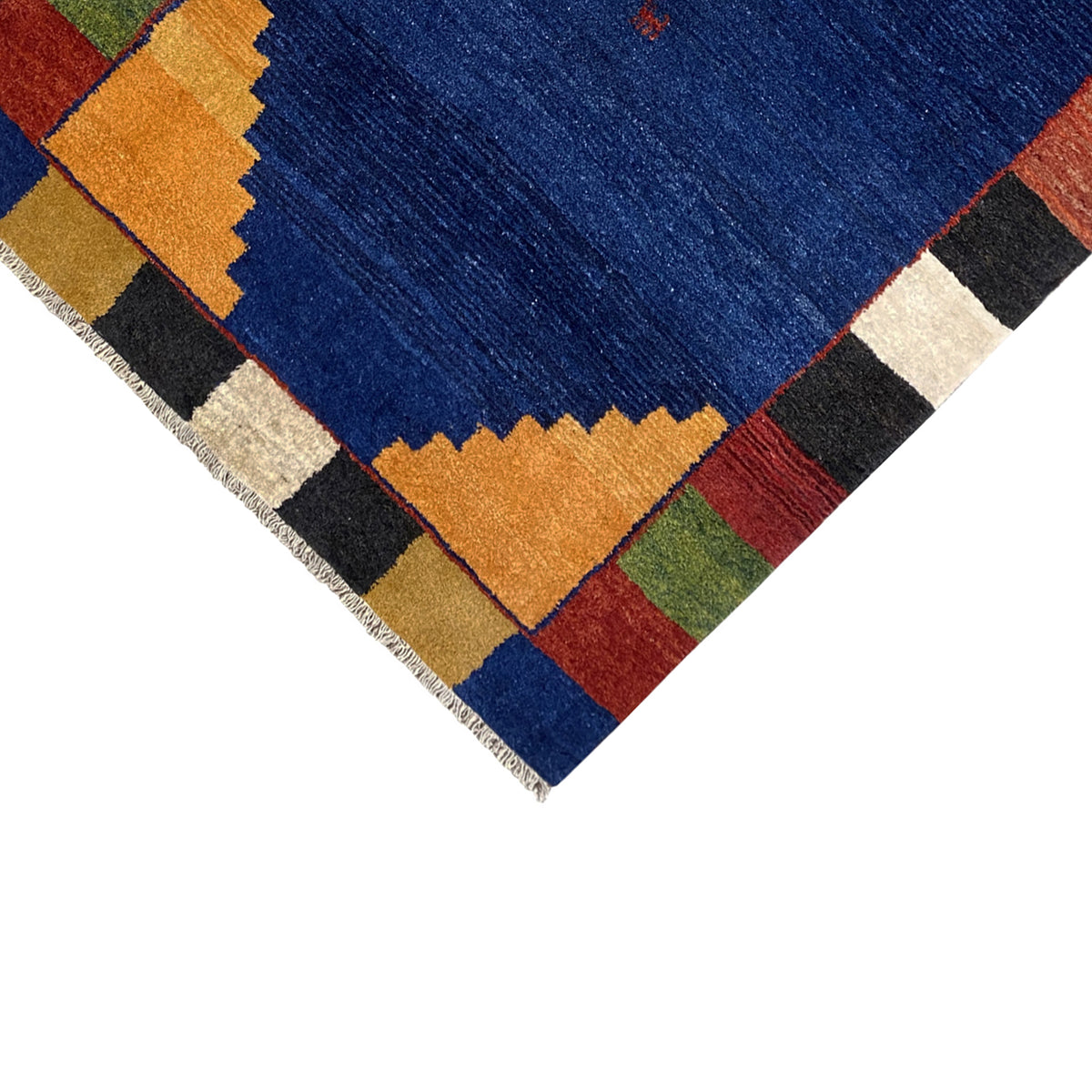 Corner section of the rug with a blue center, colorful checks, and a bound edge with fringes.