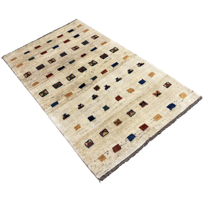 Gabbeh rug at an oblique angle: beige rug with patterned motifs and rows of quadrilaterals