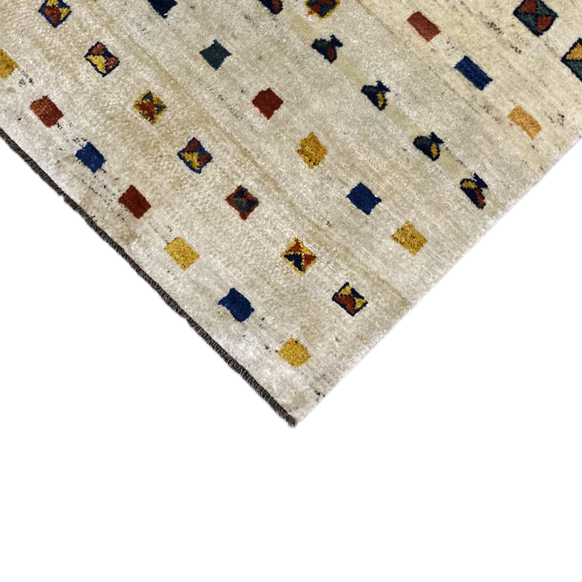 Edge view: beige Gabbeh rug with geometric quadrilaterals in blue, red, and yellow
