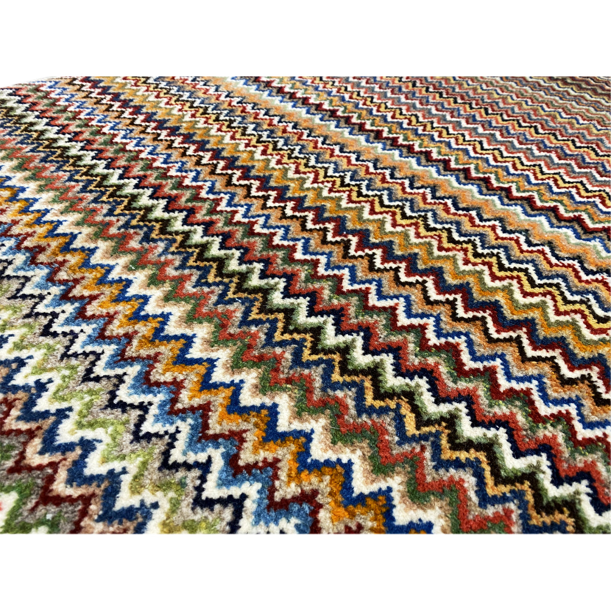 Close-up of a 130x75 cm Gabbeh rug: dense zigzag pattern in blue, green, red, and beige.