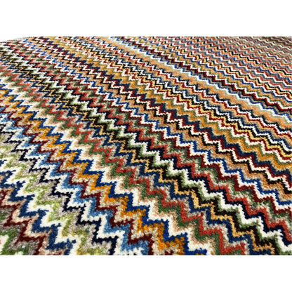 Close-up of a 130x75 cm Gabbeh rug: dense zigzag pattern in blue, green, red, and beige.