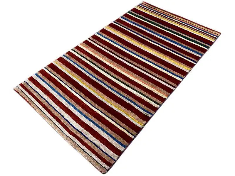 Rug, shown at an angle, striped border in shades of red, blue, and yellow
