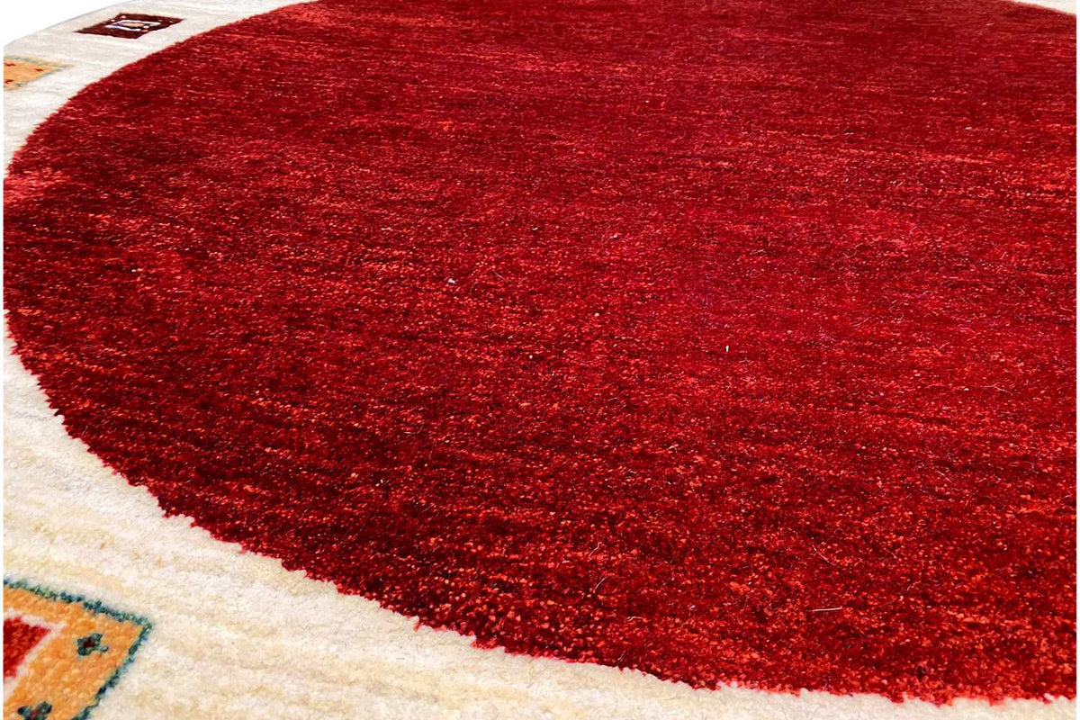 Gabbeh rug close-up: red pile field with a cream-colored border and woven corner details