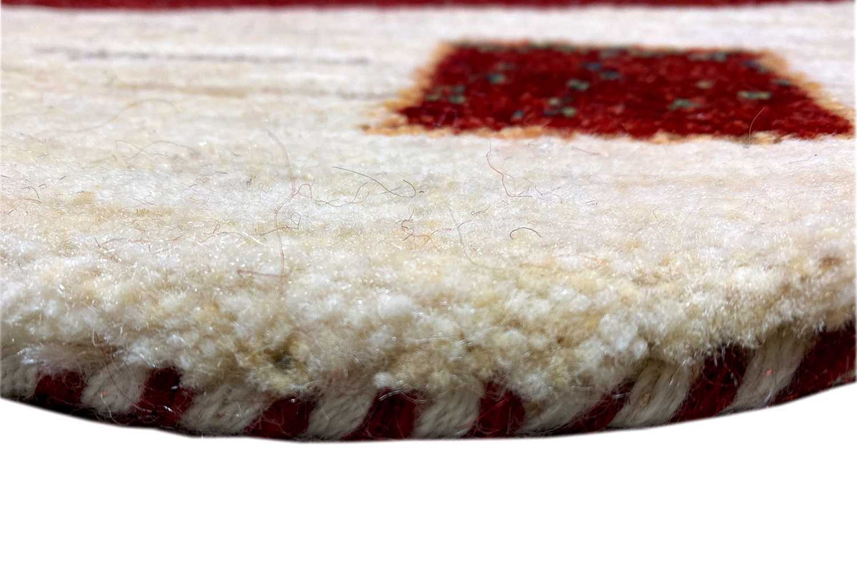 Gabbeh rug edge view with a creamy pile and a red pattern underneath