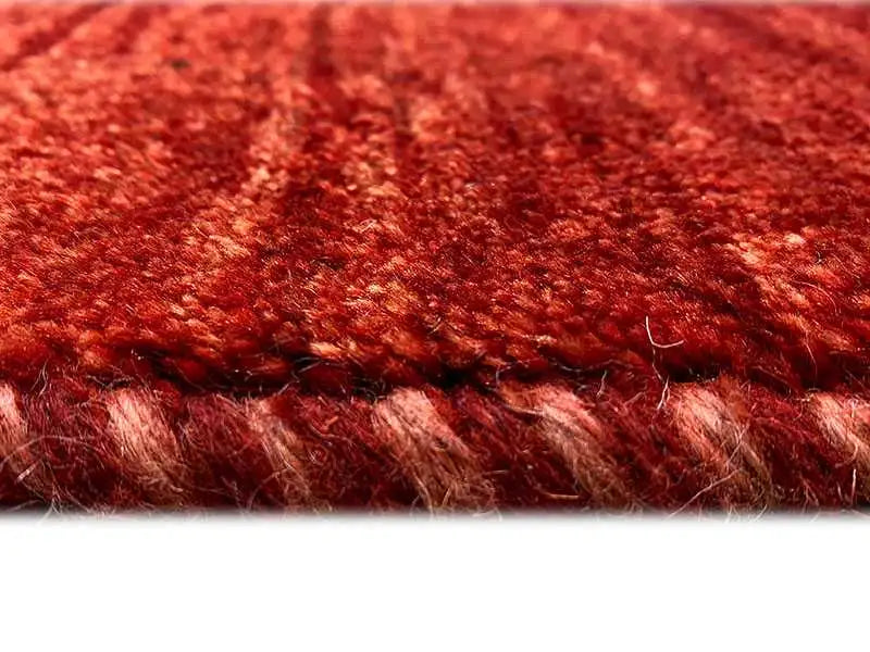 Gabbeh rug, close-up: mottled red texture, short fibers, and edge trim visible
