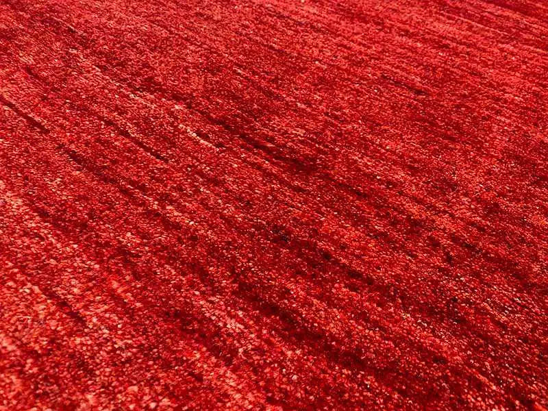 Gabbeh rug, close-up of the surface: mottled red with a fine, grainy texture