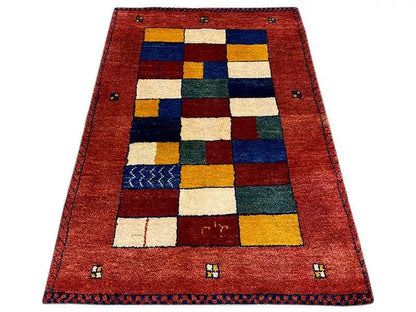 Gabbeh rug with a red background and a geometric patchwork pattern in blue, green, and yellow