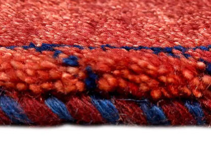 Close-up of the Gabbeh rug: red pile surface with a blue contrasting edge