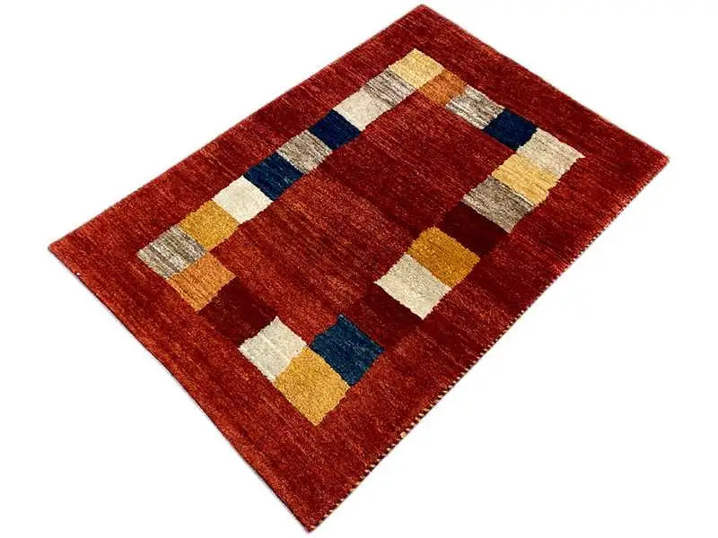 Gabbeh rug with a geometric pattern: reddish-brown field and squares in blue/beige/yellow.