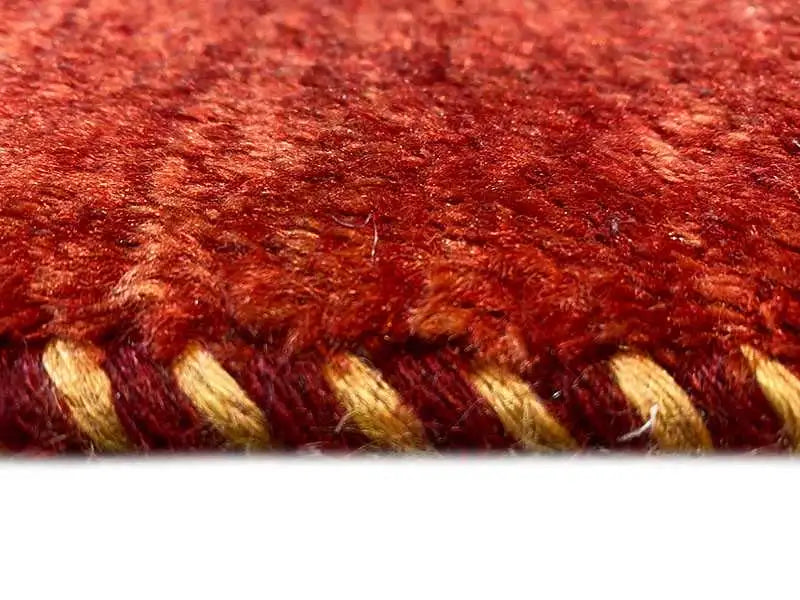 Gabbeh rug detail: reddish-brown pile with visible fiber ends at the edge.