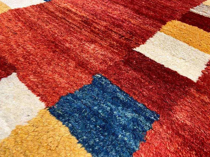 Close-up of a Gabbeh rug: reddish brown with white, yellow, and blue patterned areas.