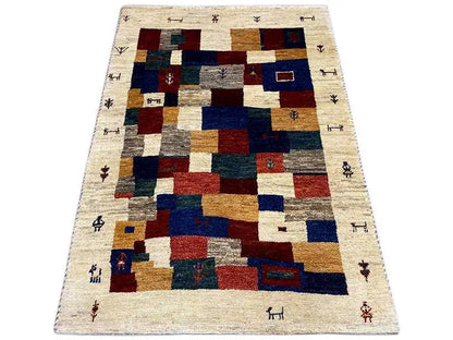 Gabbeh rug with a geometric patchwork pattern, beige background, and shades of blue, red, and green.