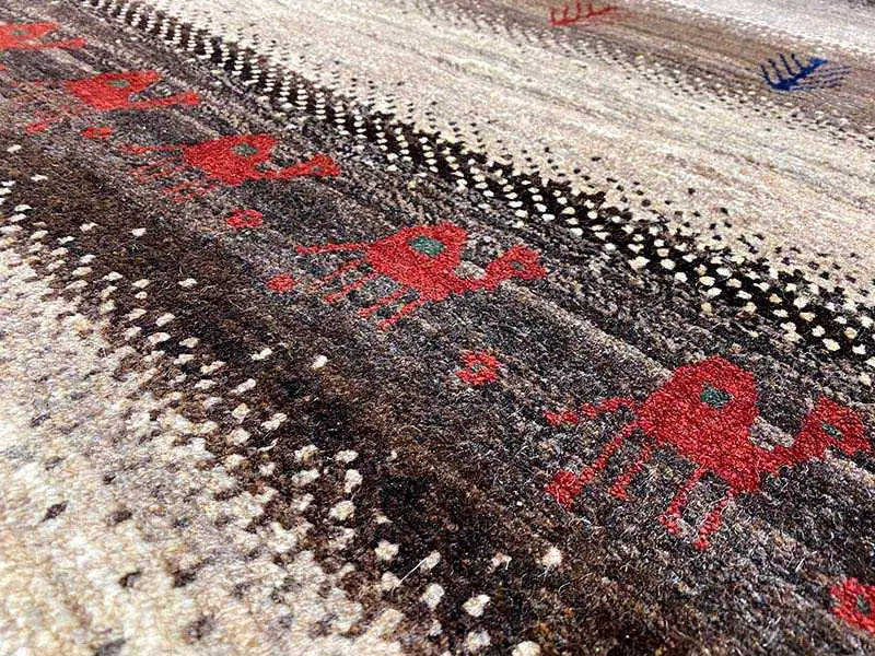 Gabbeh rug close-up: red diamonds, black dot patterns, and a beige background