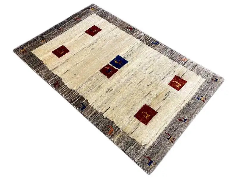 Gabbeh rug in oblique view: light-colored surface with red and blue tile motifs, gray border