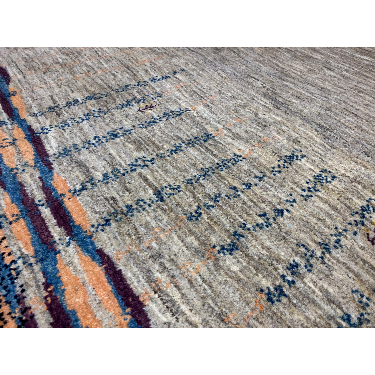 Close-up of a Gabbeh rug: gray pile with rows of blue dots and orange accents