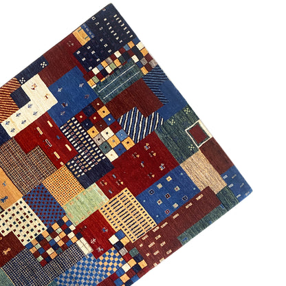 Gabbeh rug at an angle: Patchwork tiles in blue, red, green, and beige with small symbols